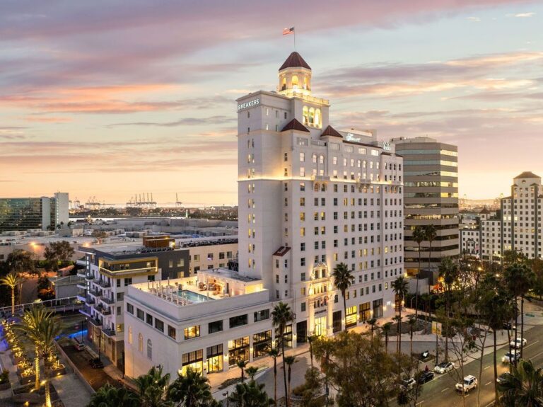Historic high-rise hotel lit at dusk after restoration, with a new rooftop pool terrace below