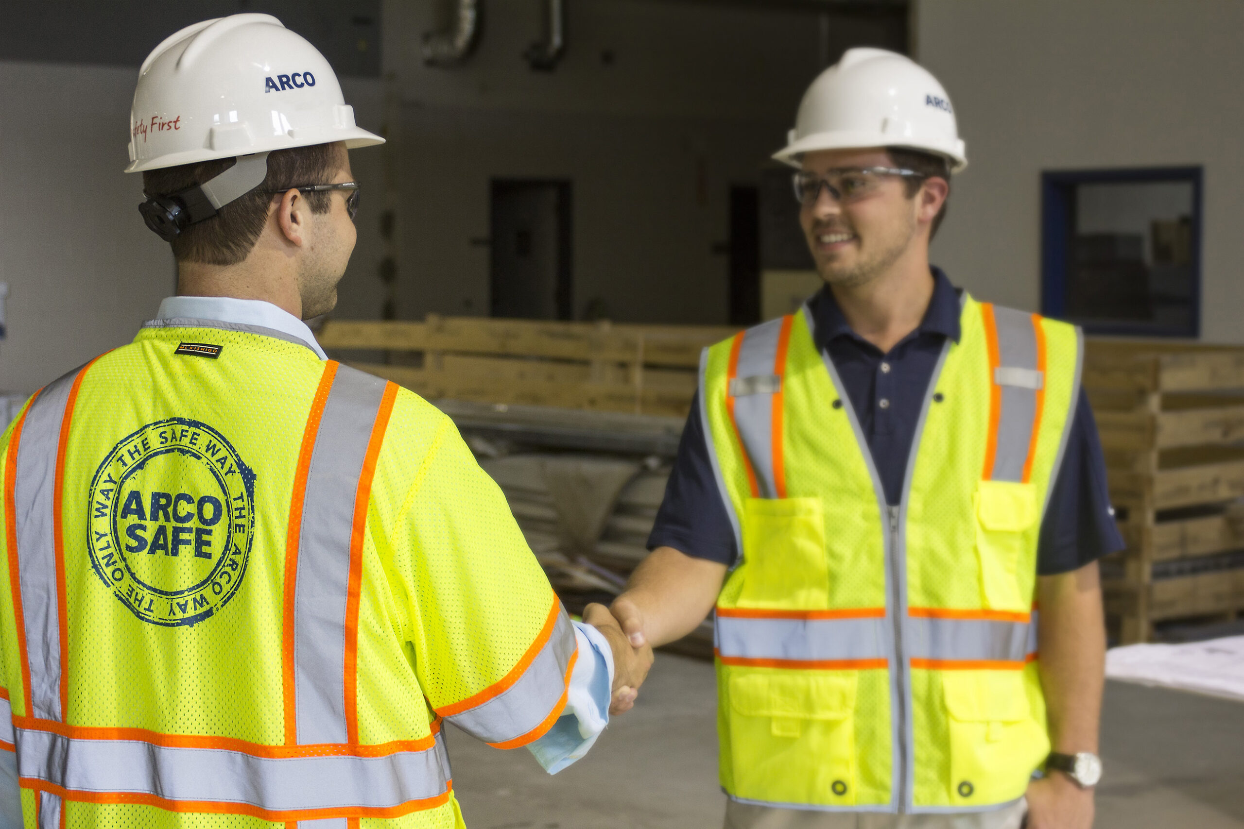 ARCO team member in a safety vest and hard hat shaking hands with a client on a job site