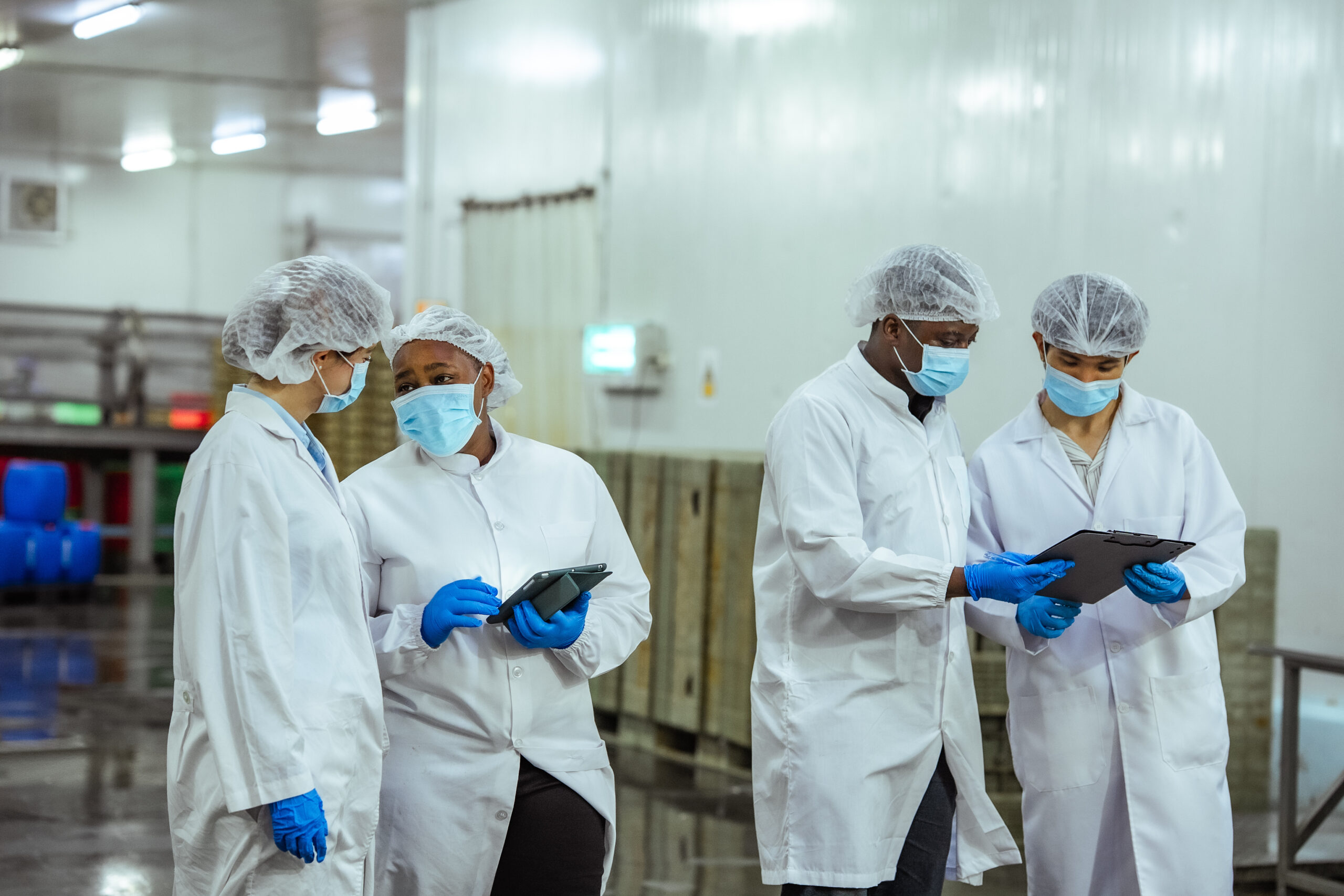 Food plant team in hairnets, masks and lab coats reviewing plans on tablets in a processing facility